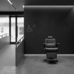 Modern, bicolor salon interior in dark and medium grey. Empty barber chair, accessibility ramp, and PMR symbol convey safety and compliance.