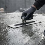 Un artisan lissant du béton frais avec une taloche métallique sur un chantier.