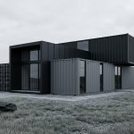 Maison architecturale noire construite à partir de containers maritimes dans un paysage naturel.