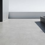 Une terrasse moderne en béton gris lisse avec un bac à plantes minimaliste sous un ciel lumineux.