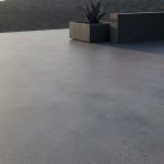 Une terrasse moderne en résine grise avec un pot de fleurs, offrant une vue dégagée sur un paysage vallonné.