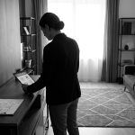 Une femme en tenue professionnelle consulte une tablette numérique devant des plans de logement dans un salon moderne.